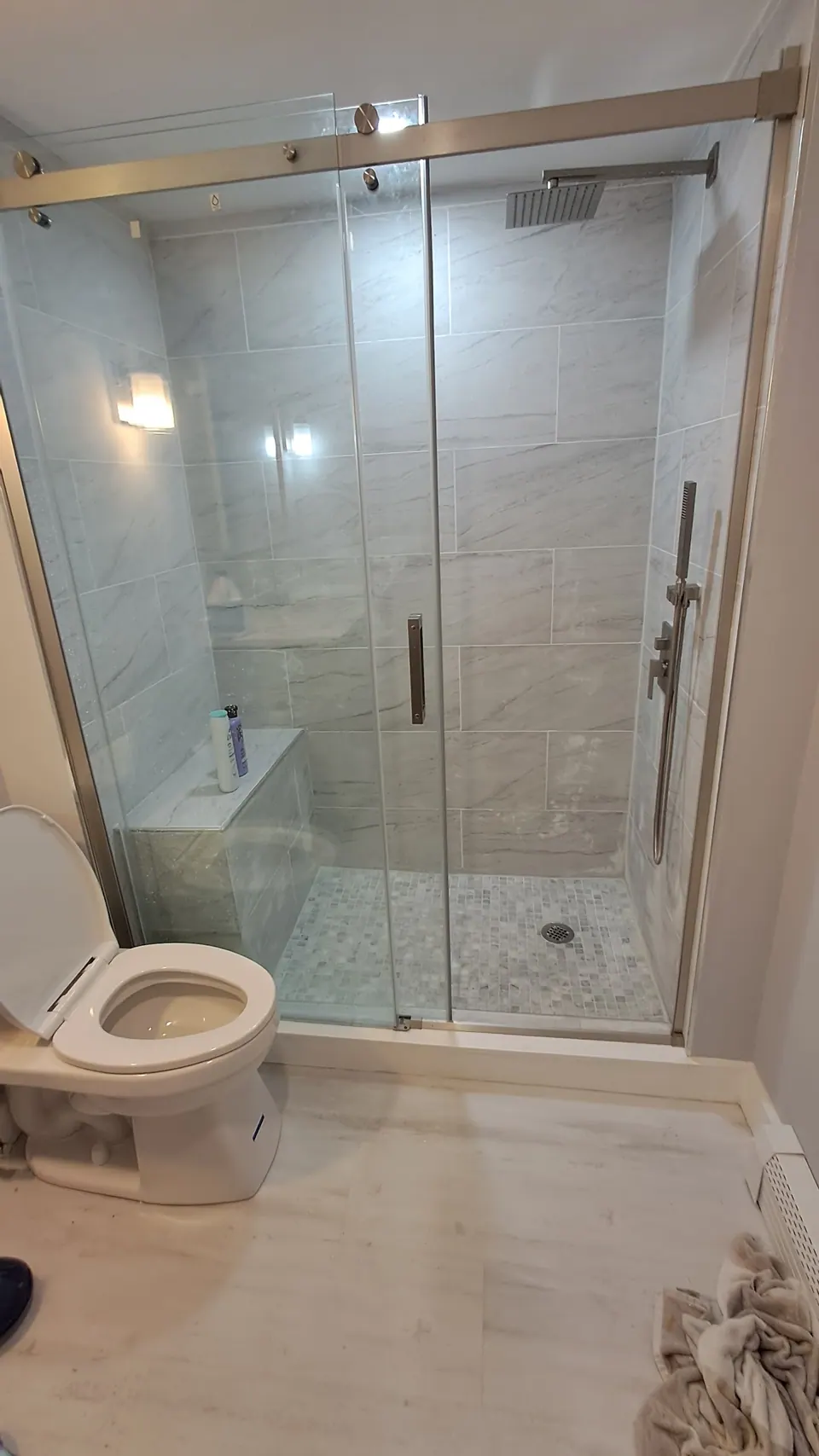 Walk-in shower with a bench and sliding glass door next to the toilet.