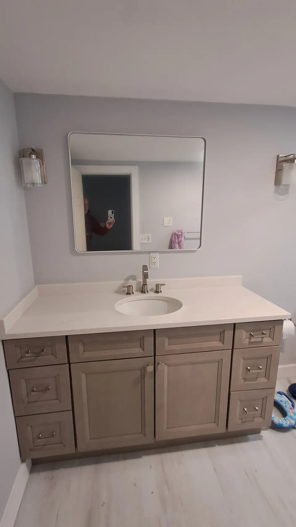 Finished bathroom: greige shaker vanity, white top and a round-cornered mirror.