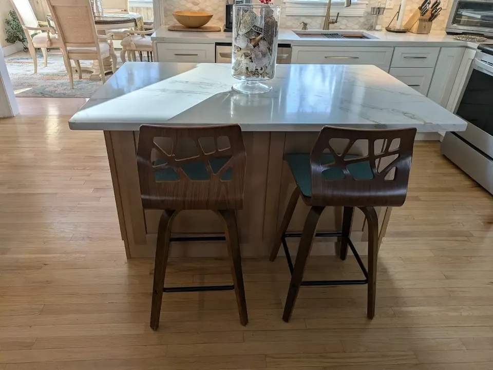 Natural wood island with white veined countertop and two stools, white cabinets and range behind.