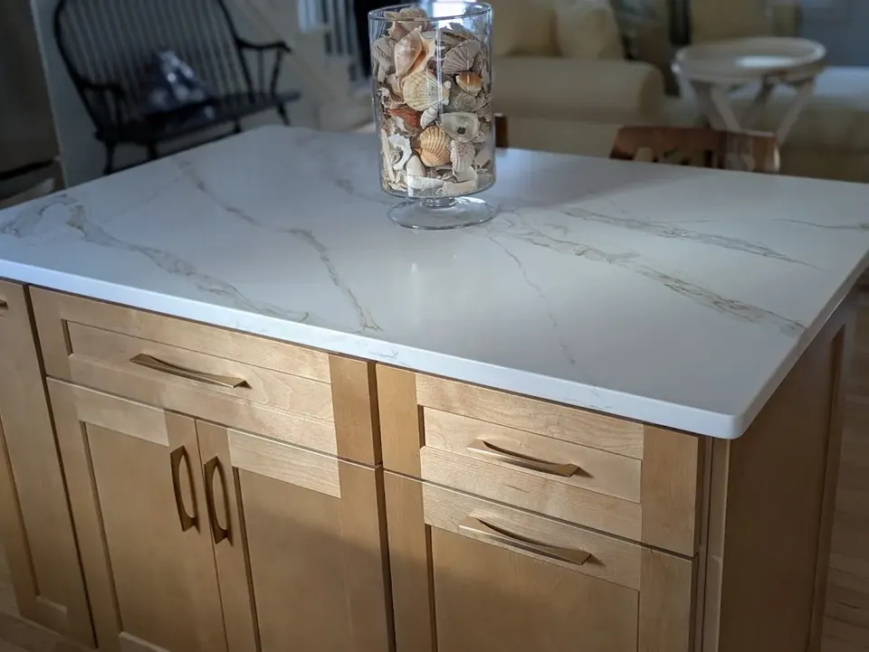 Natural wood island with drawers and doors, gold pulls and a white veined countertop.
