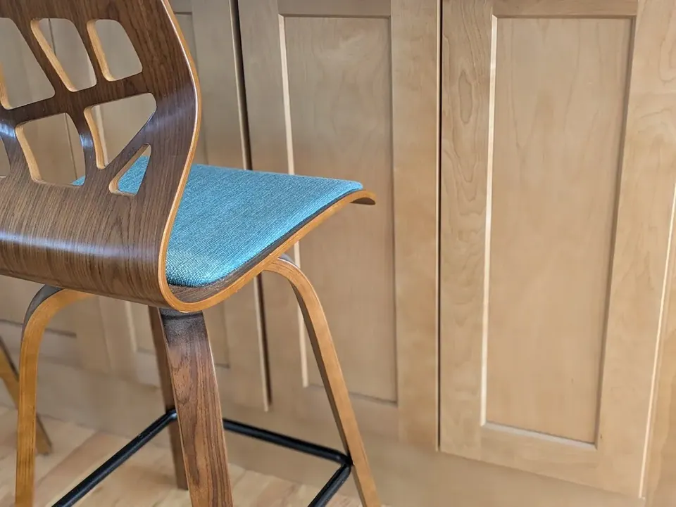 Wood counter stool with teal seat in front of natural wood shaker panels.