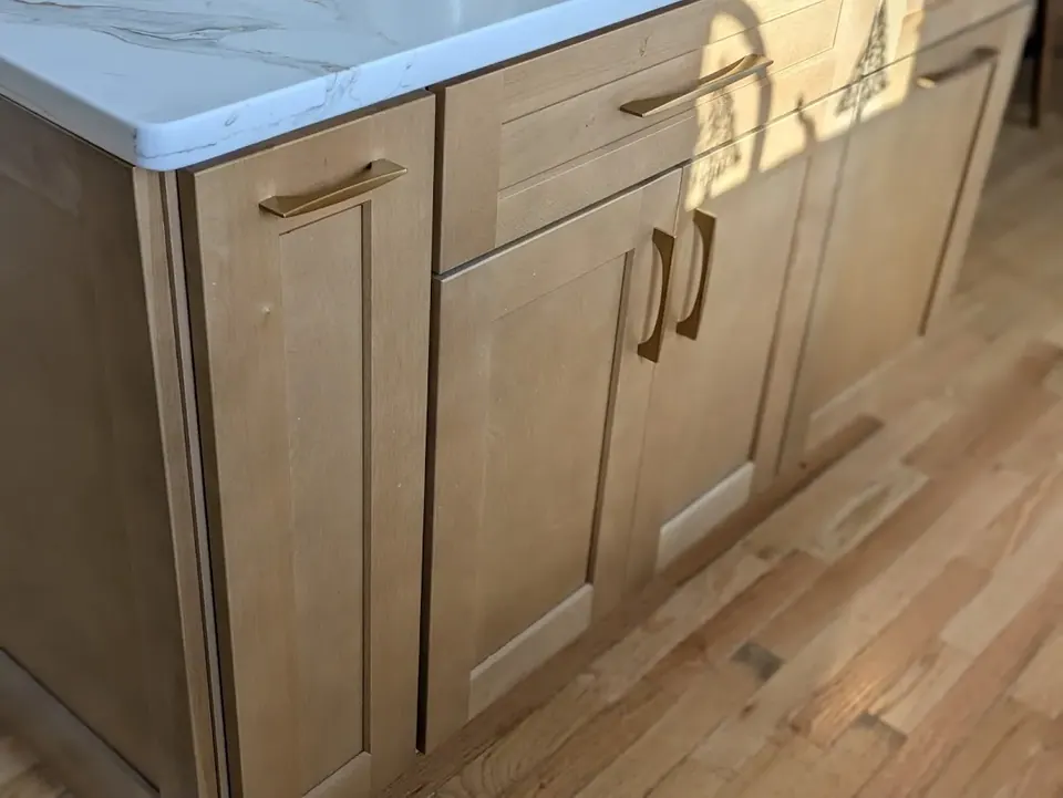 Natural wood shaker doors and drawers with gold pulls under the white countertop.