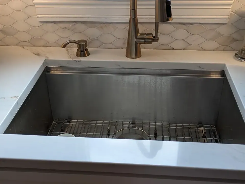 Empty stainless undermount sink with gold-tone faucet, white countertop and tile backsplash.