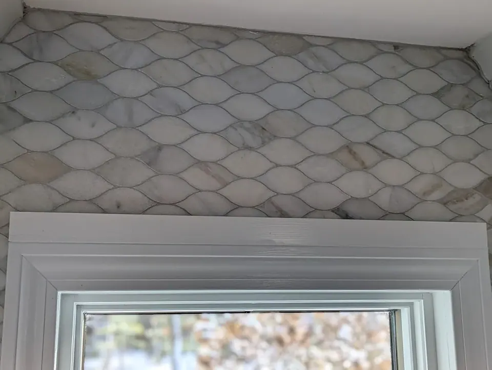 White leaf-shaped tile backsplash with gray veining above the white window trim.