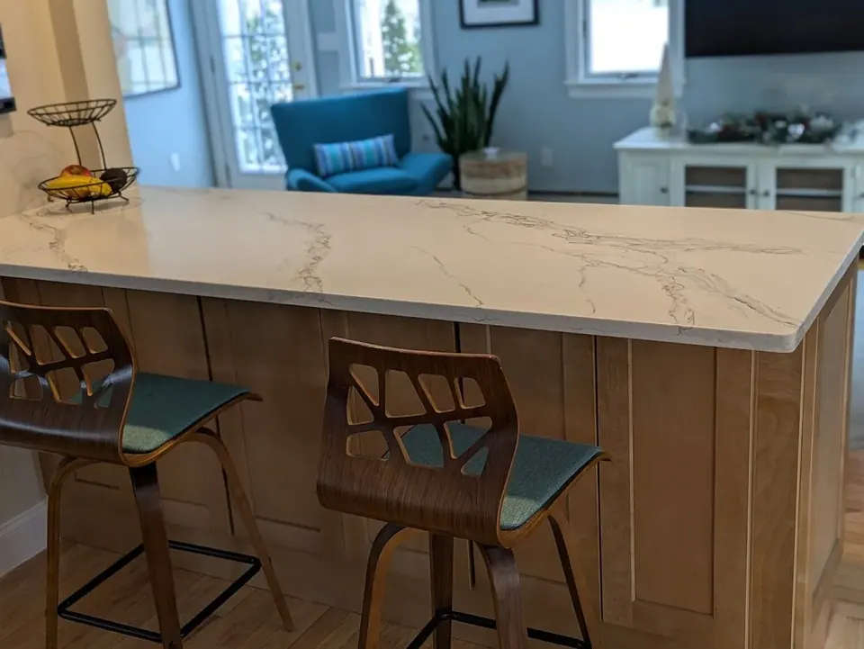 White veined peninsula countertop over natural wood shaker panels with two stools.