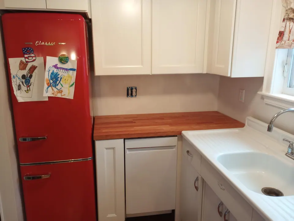 White shaker wall cabinets over a butcher-block counter, between a red retro refrigerator and a white drainboard sink.