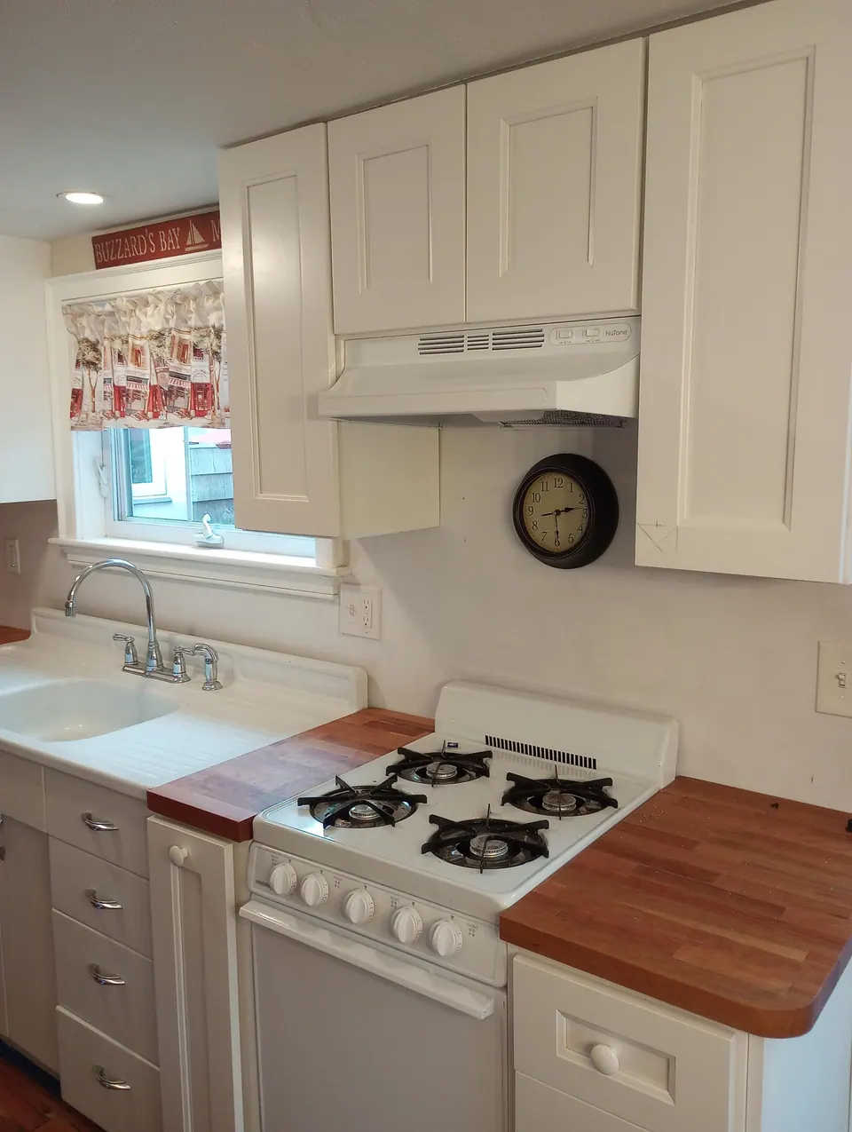 White shaker wall cabinets and a range hood above a white gas range, flanked by butcher-block counters.