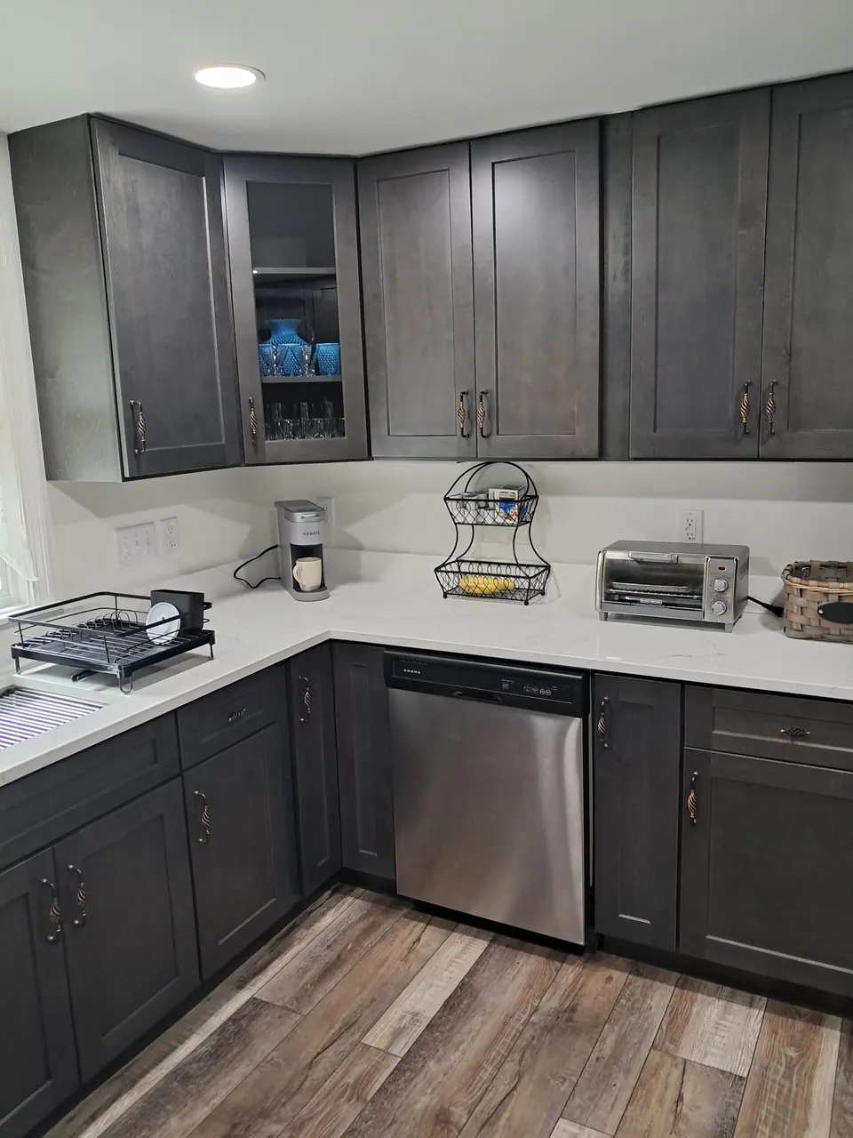 Dark gray shaker wall and base cabinets around a corner with a glass-front cabinet and stainless dishwasher.