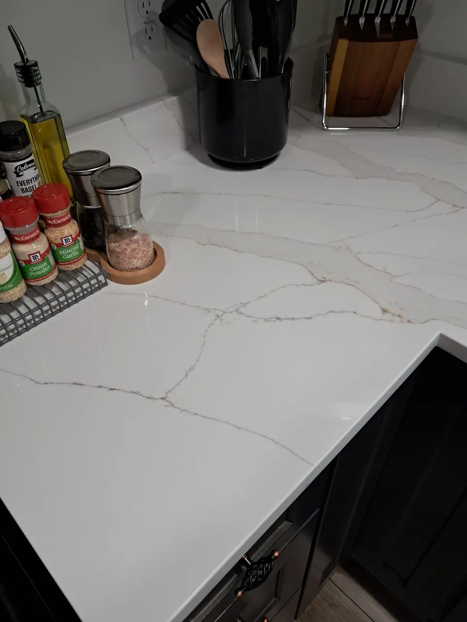 White countertop with thin gray and gold veining, holding spice jars, a utensil crock and knife block.