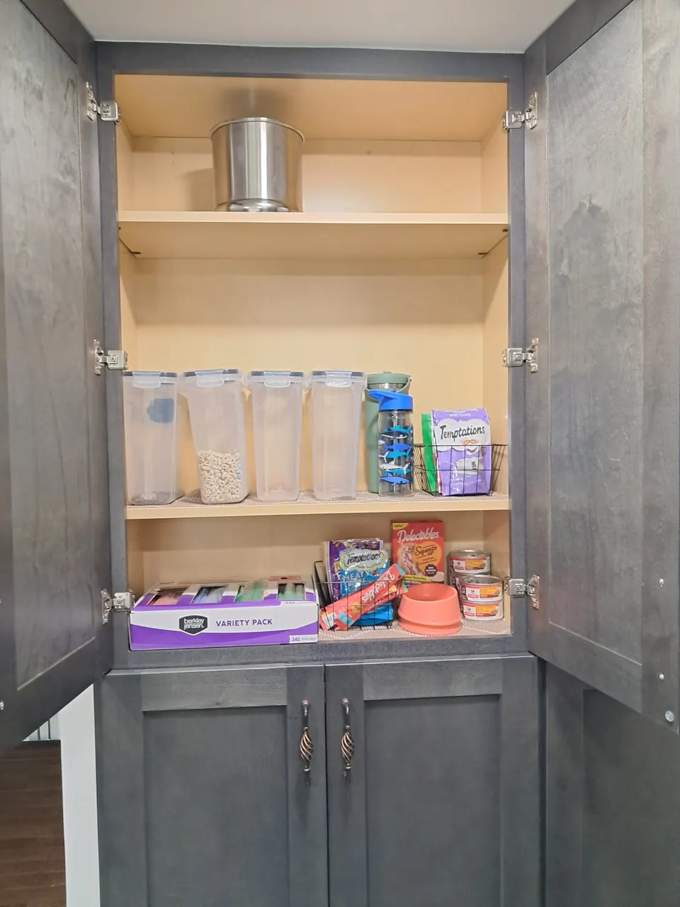 Tall dark gray pantry cabinet with upper doors open, showing light-toned interior shelves with containers.