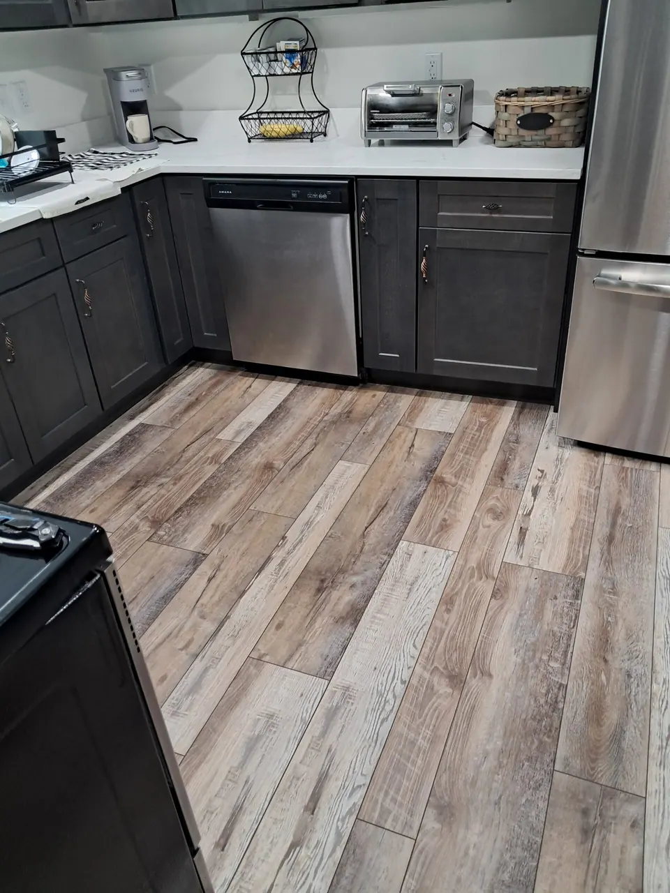 Dark gray base cabinets and stainless dishwasher seen across a wood-look plank floor.