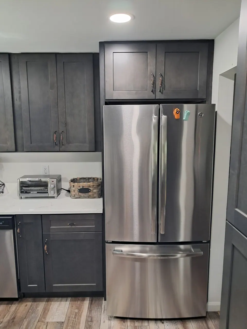 Stainless French-door refrigerator with a dark gray cabinet above and wall and base cabinets beside it.