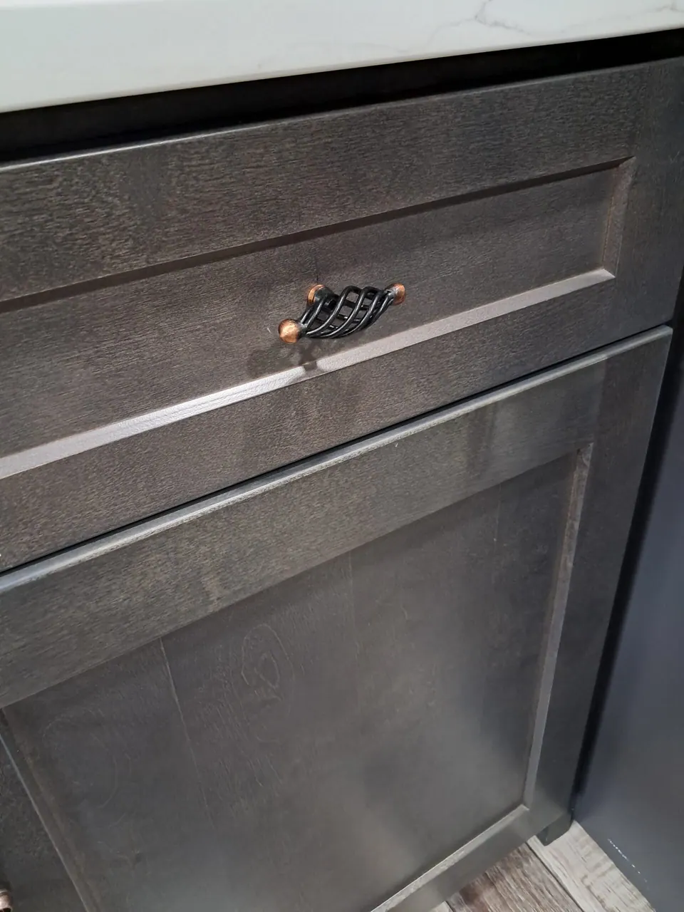Close-up of a dark gray shaker drawer front with a twisted black and copper pull.