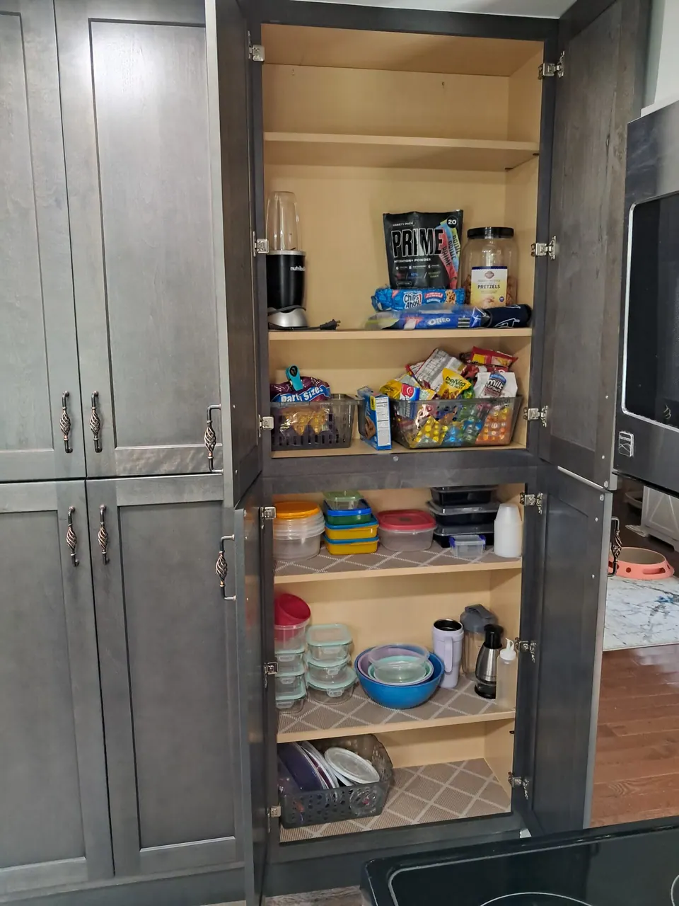 Dark gray pantry cabinet with upper and lower doors open, showing shelves of food and storage containers.