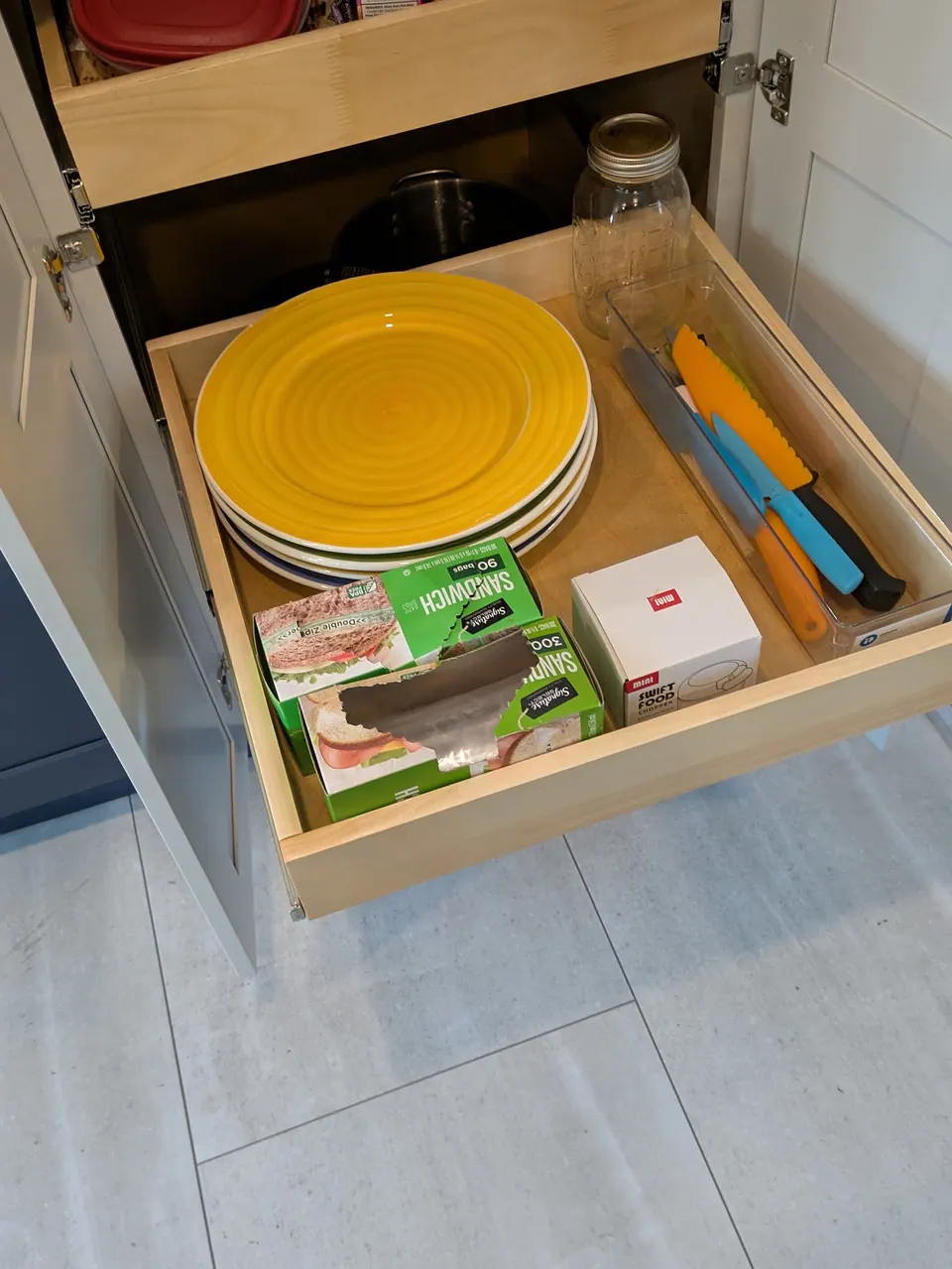 Roll-out tray pulled from the light gray pantry cabinet, holding plates and boxes of food bags.