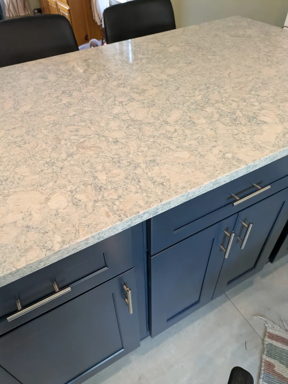 Cream countertop with gray veining on the navy blue peninsula, doors and drawers with bar pulls below.