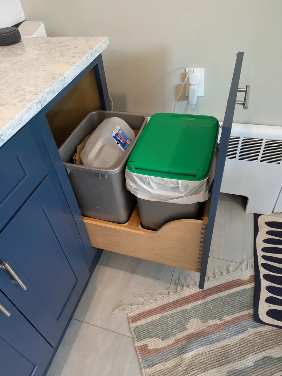 Pull-out trash cabinet open at the end of the navy blue peninsula with two waste bins.