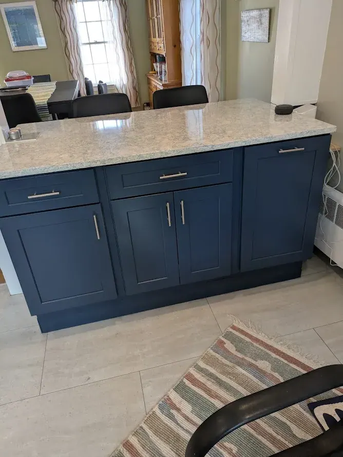 Navy blue shaker peninsula with bar pulls under a cream countertop with gray veining, dining room beyond.