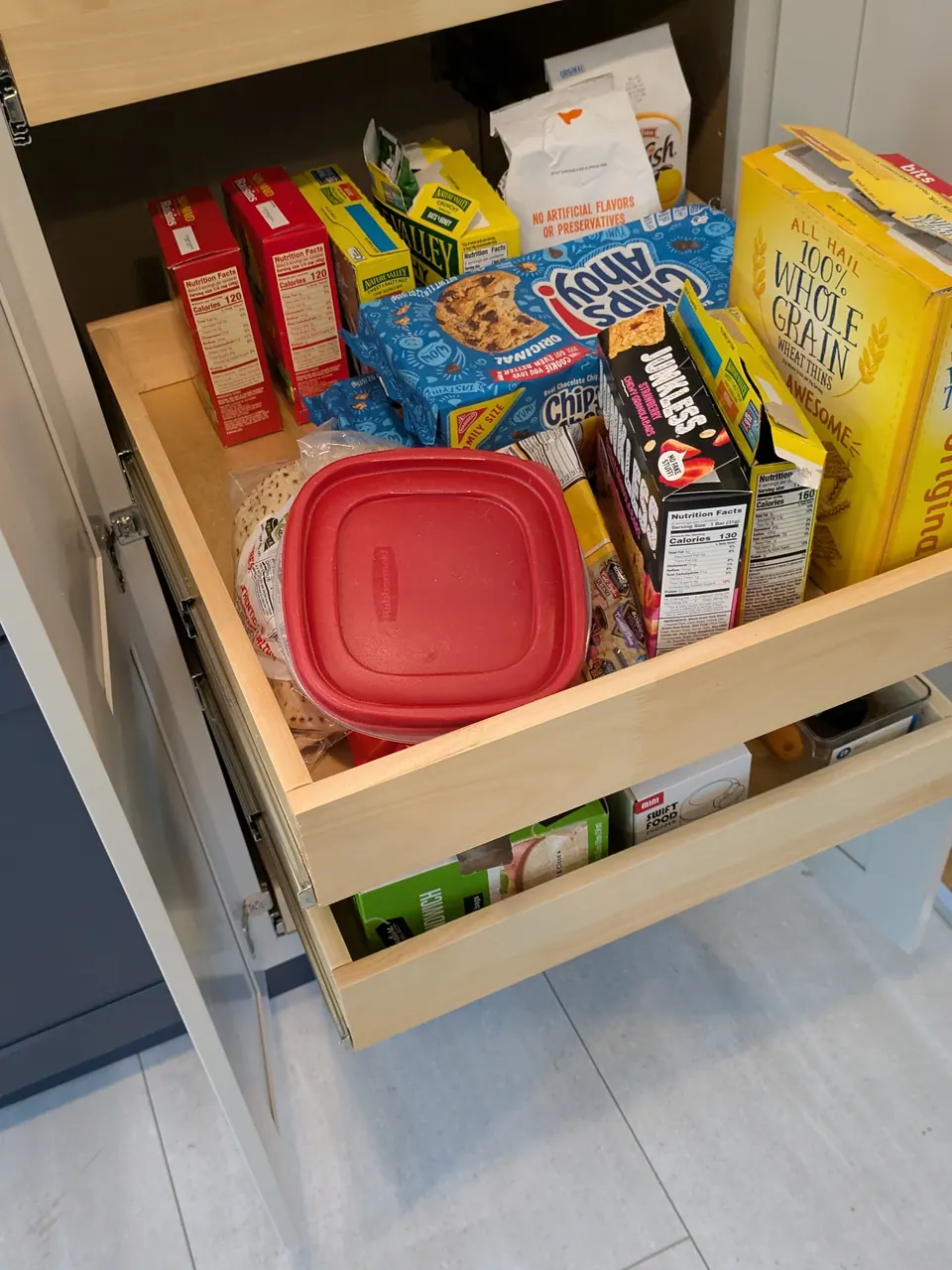 Roll-out trays in the light gray pantry cabinet filled with boxed snacks and food containers.