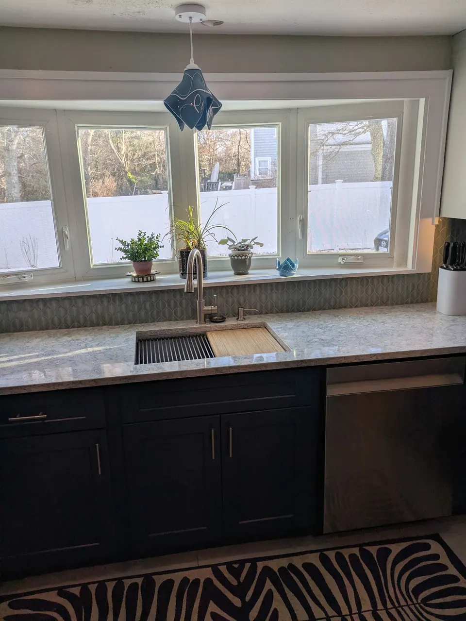 Navy blue sink base cabinets and stainless dishwasher under a wide window with potted plants.