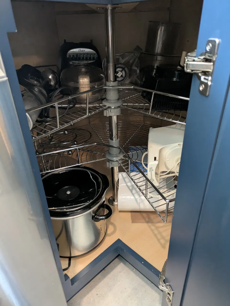 Navy blue corner base cabinet open, showing a two-tier wire lazy Susan with pots and a slow cooker.