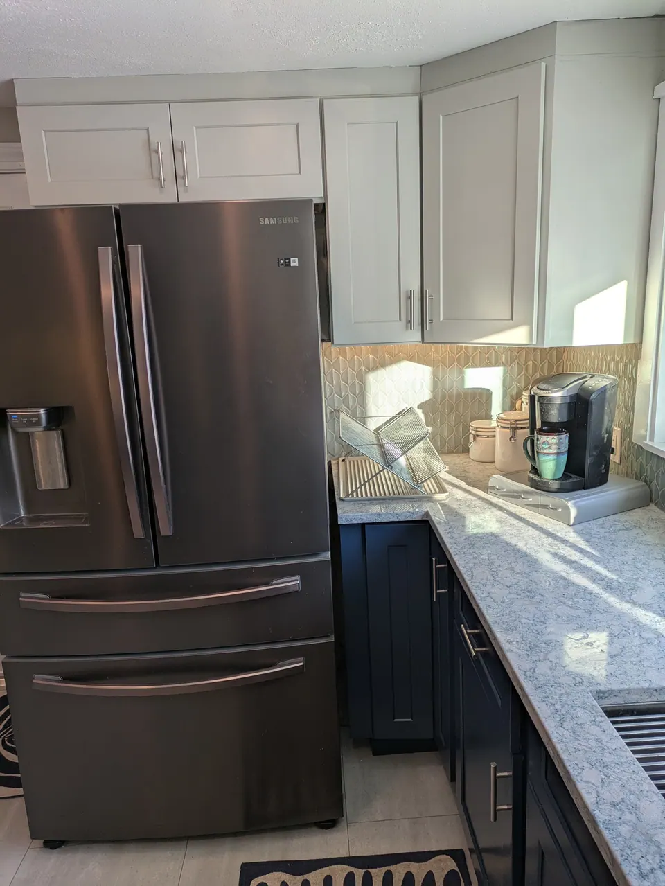 Dark stainless French-door refrigerator with light gray wall cabinets above and navy base cabinets along the counter.