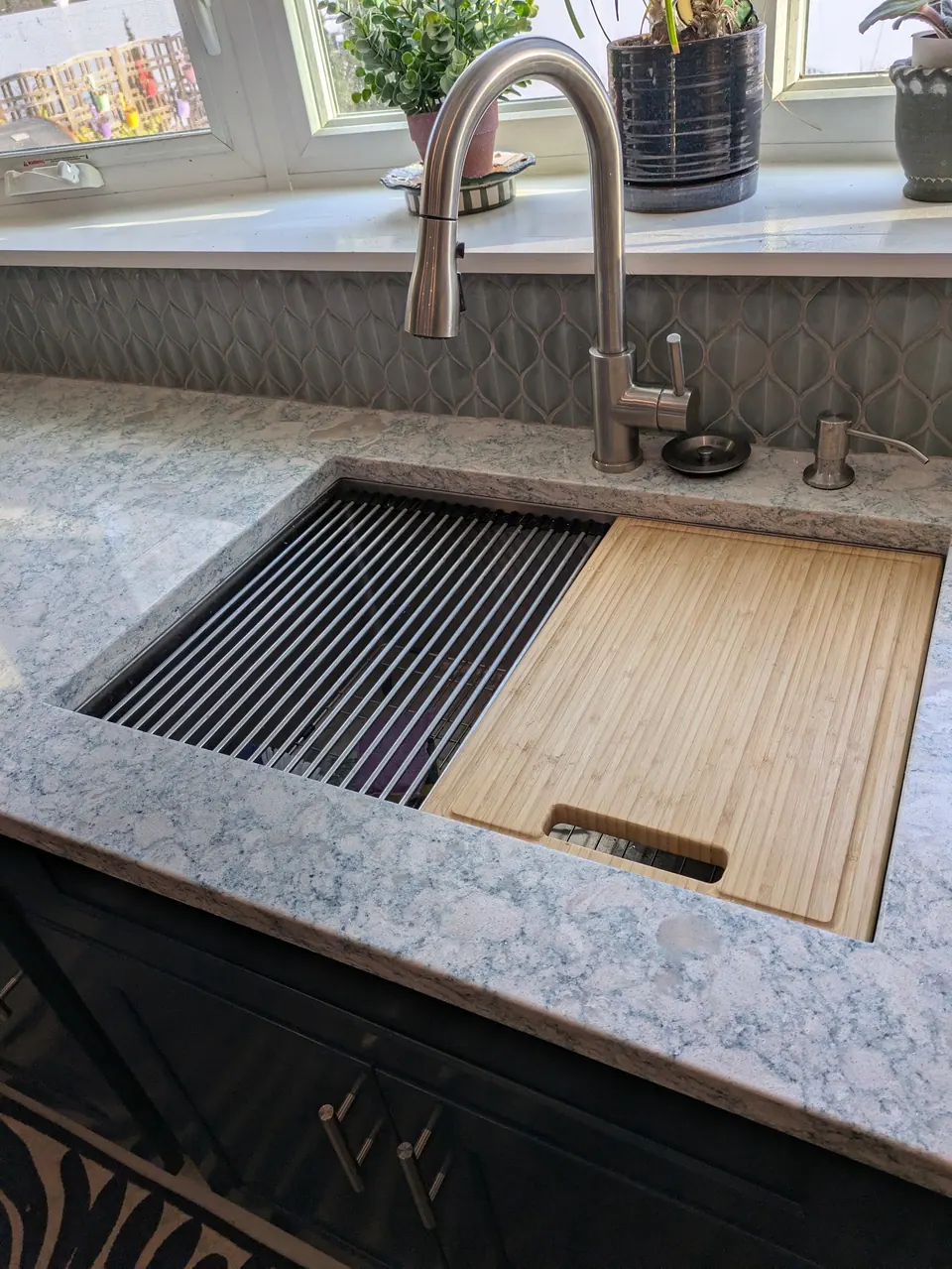 Undermount workstation sink with roll-up drying rack and wood cutting board, pull-down faucet behind.
