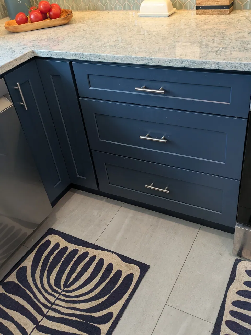 Navy blue three-drawer base cabinet beside the corner cabinet under the cream veined countertop.
