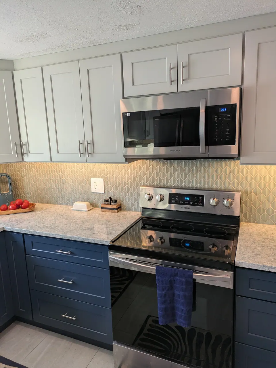 Light gray wall cabinets and over-the-range microwave above a stainless range and navy blue drawer bases.