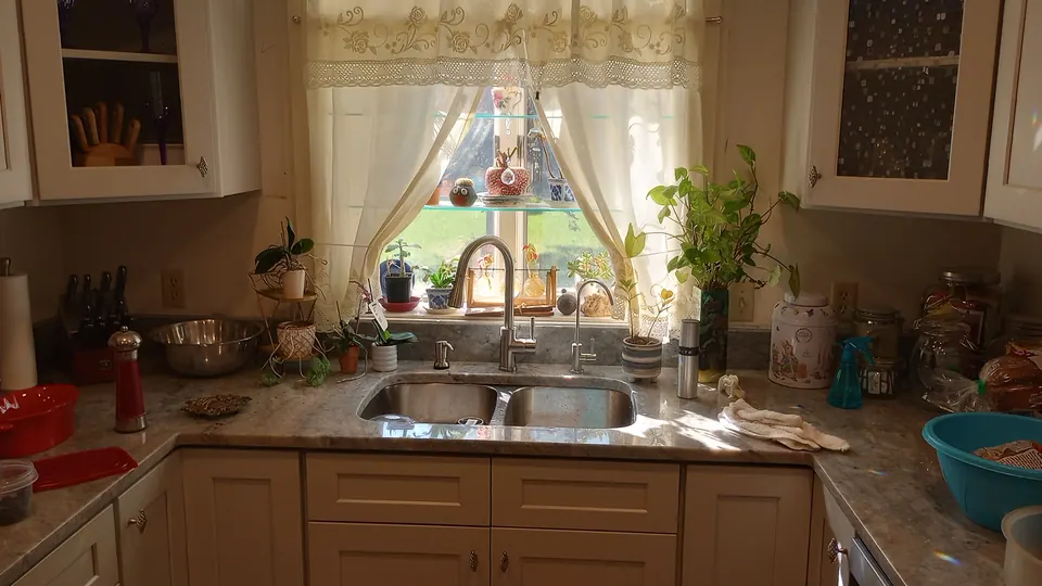 Sink under the window between light gray shaker cabinets with glass-front corner cabinets.