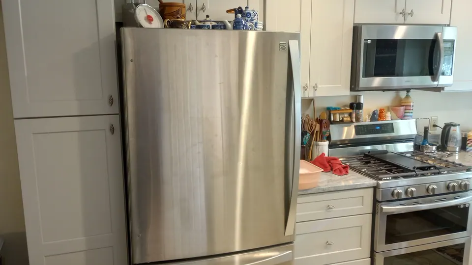 Stainless refrigerator beside a tall light gray pantry cabinet and the range wall.