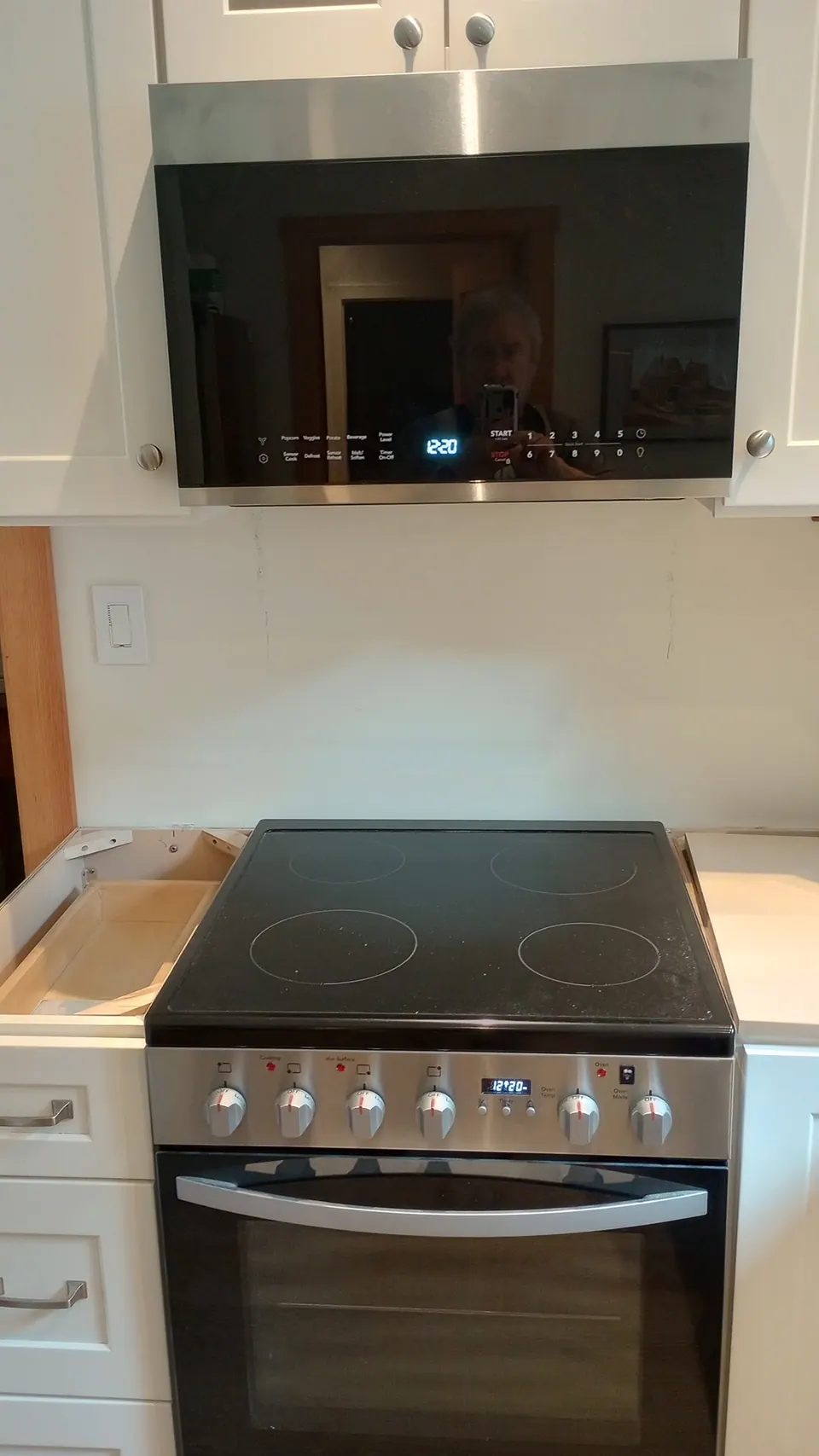 New range under the microwave between light gray cabinets, counter not yet set.