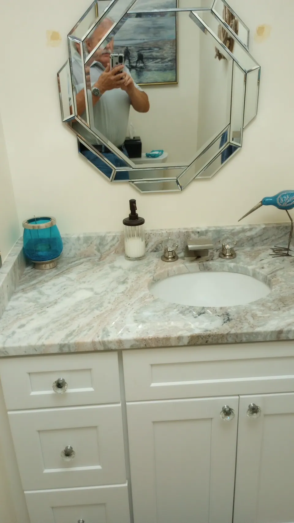 White shaker vanity with a granite top and an octagonal mirror.
