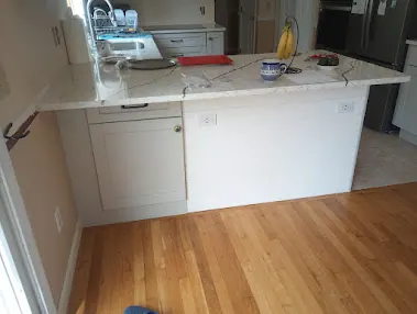 Peninsula with white veined countertop and white plank-paneled back, kitchen beyond, light wood floor in front.