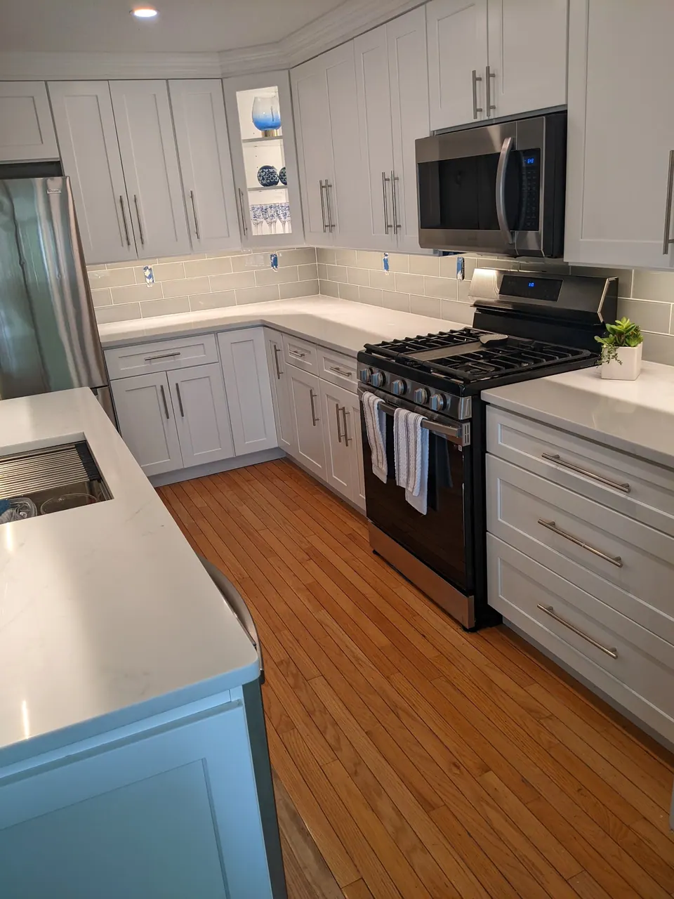 Light gray shaker kitchen with a white quartz counter, gas range and microwave.