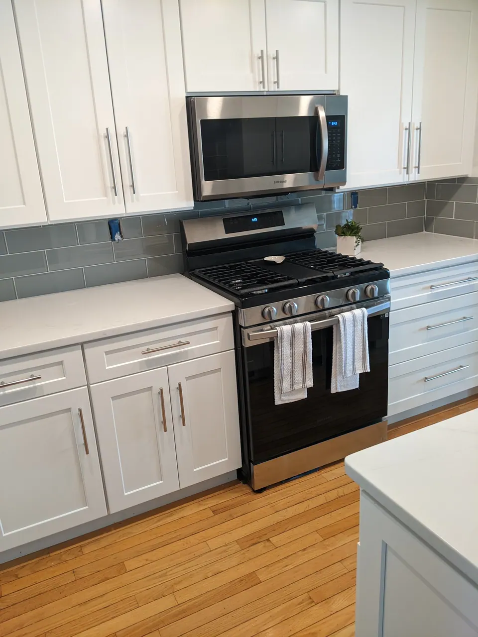 Range wall of light gray shaker cabinets with a gray glass tile backsplash.