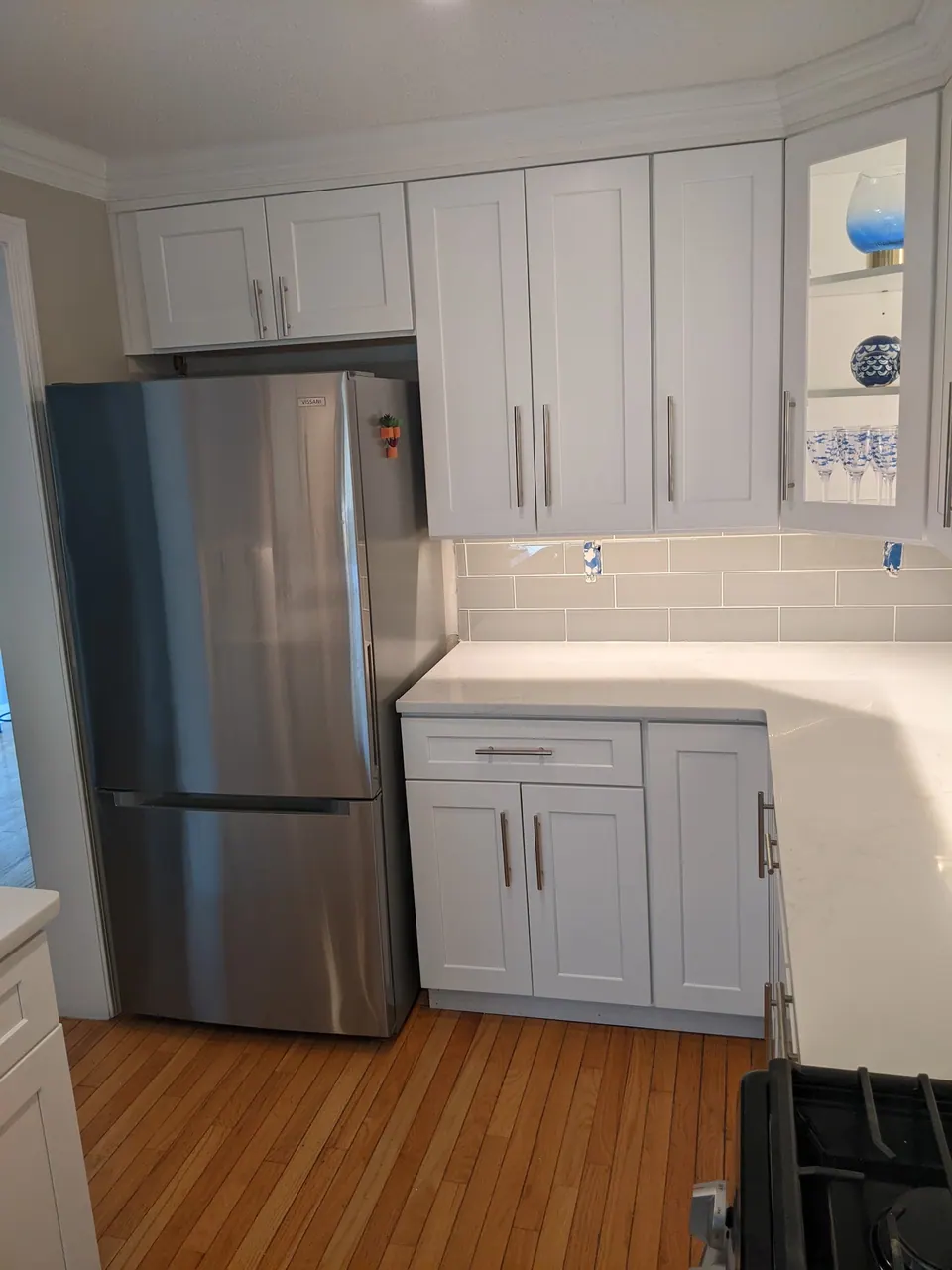 Refrigerator beside light gray cabinets and a glass-front corner cabinet.