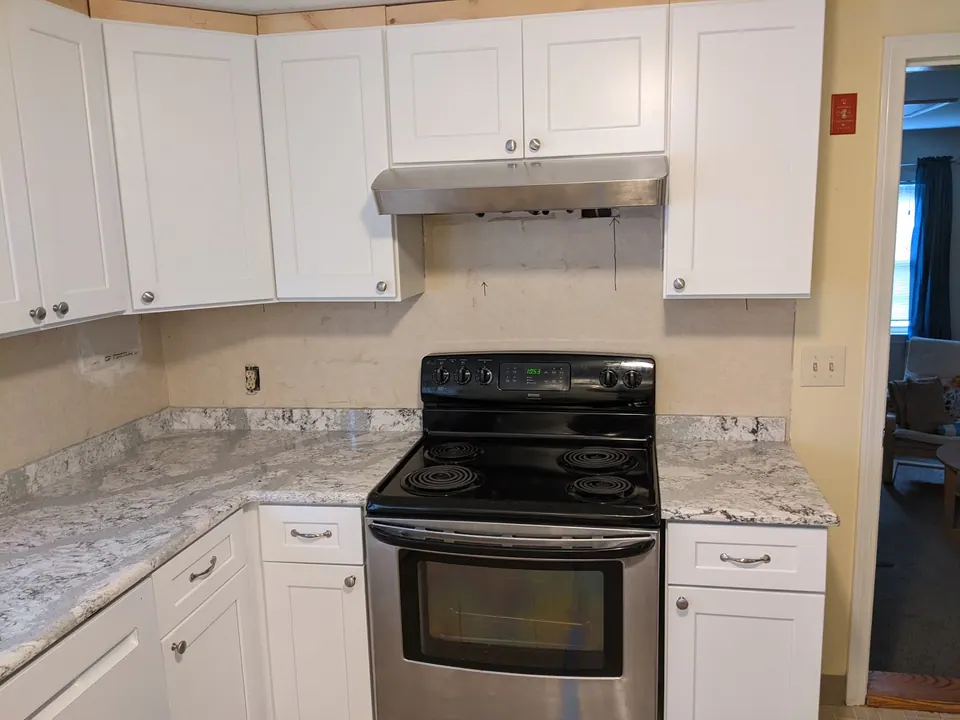 White shaker cabinets around the range with a range hood and granite counters.