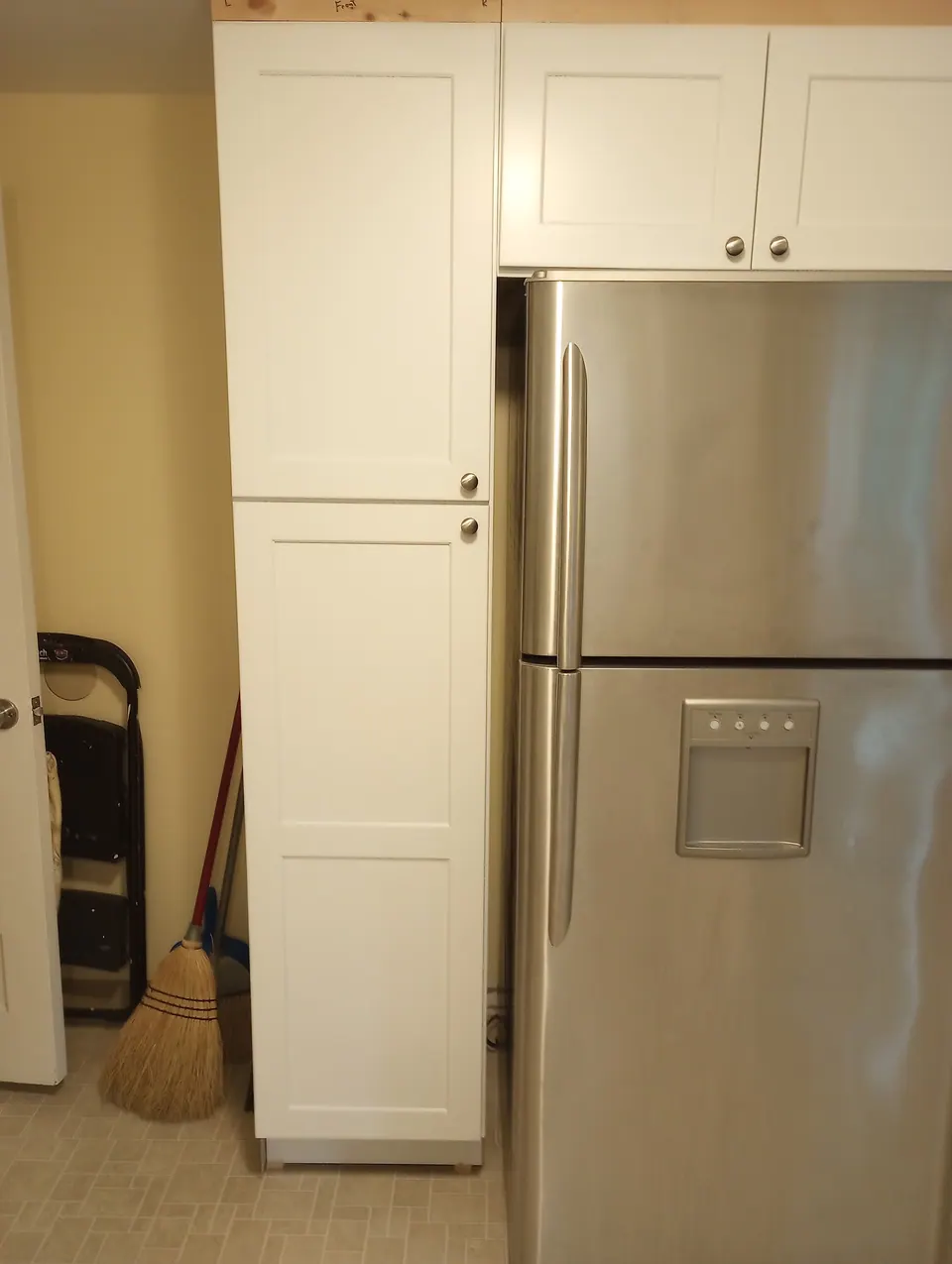 Tall white pantry cabinet beside the refrigerator with wall cabinets above.