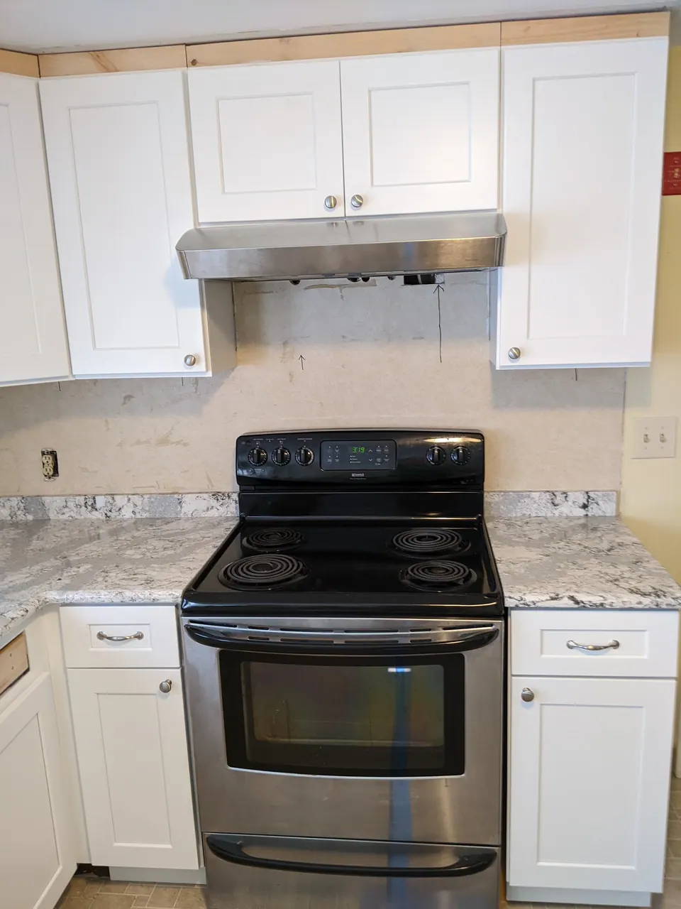 Range wall with white shaker cabinets and a hood, counter newly set.