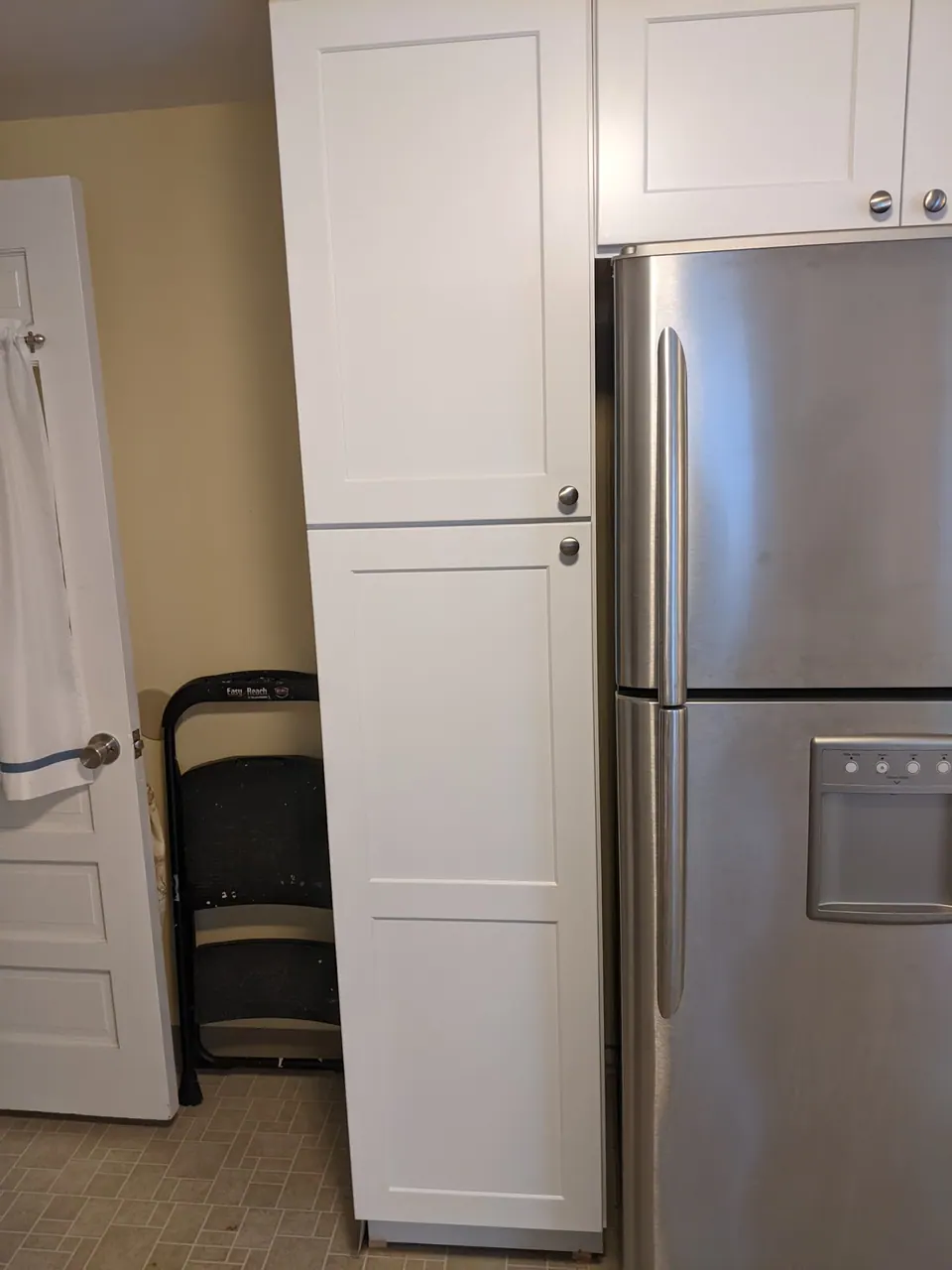 Tall white pantry next to the stainless refrigerator.