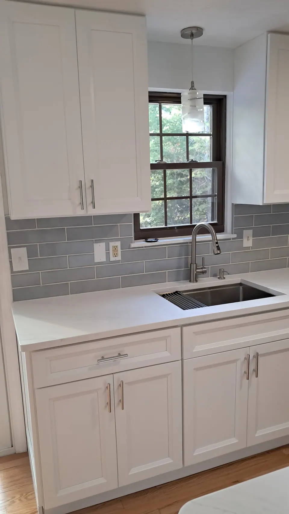 Sink under the window between white shaker cabinets with a gray-blue subway tile backsplash.