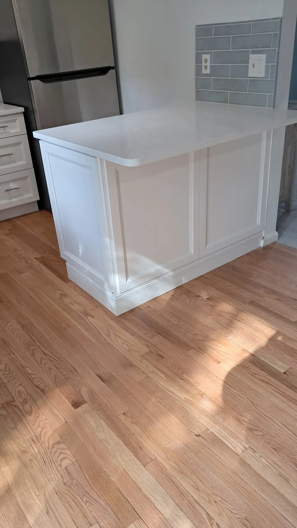 Island end with a raised panel and a white quartz top, the refrigerator behind.