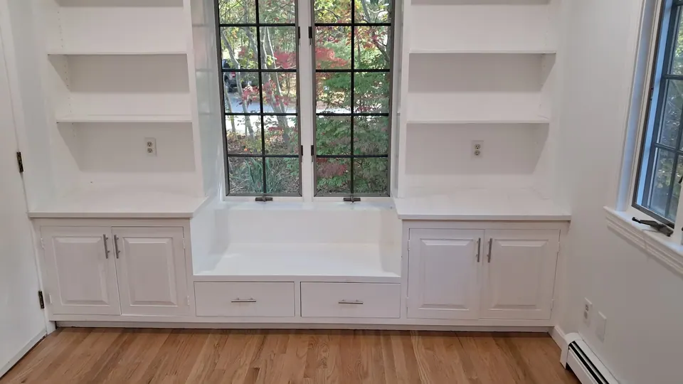 Dining room window seat with drawers between white cabinets and open bookcases.