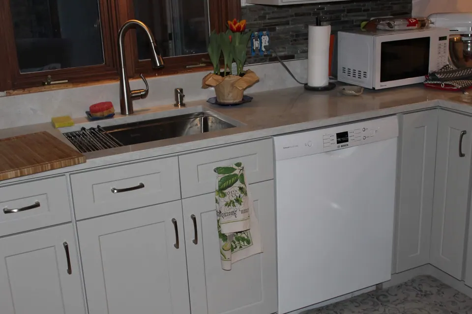 Sink run of light gray shaker cabinets with a white dishwasher and a stone-look counter.