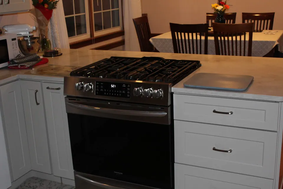 Gas range between light gray shaker base cabinets, dining room beyond.