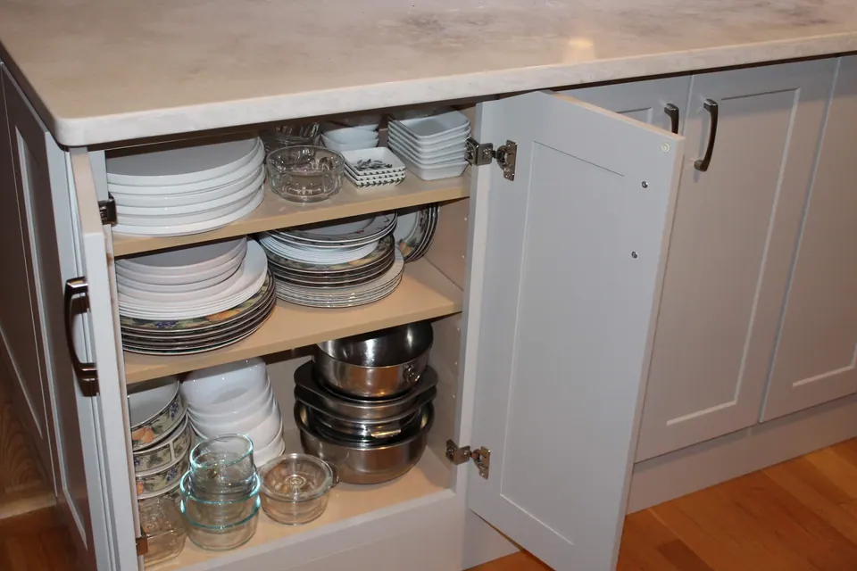 Light gray base cabinet open with dishes and pots inside.