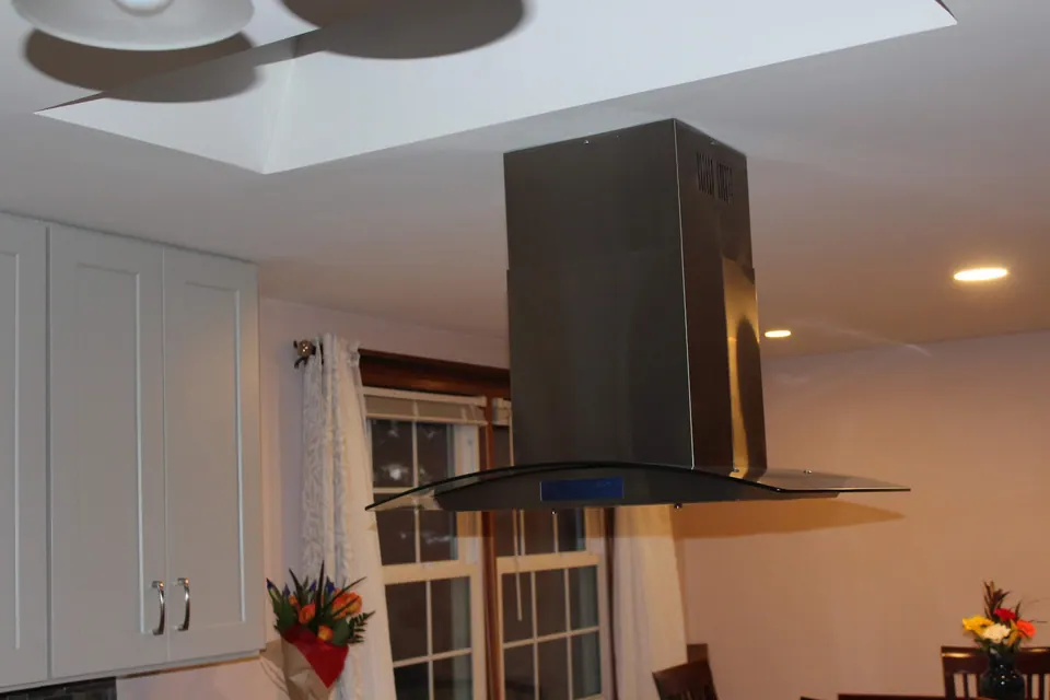 Stainless chimney hood over the cooktop in a light gray kitchen.