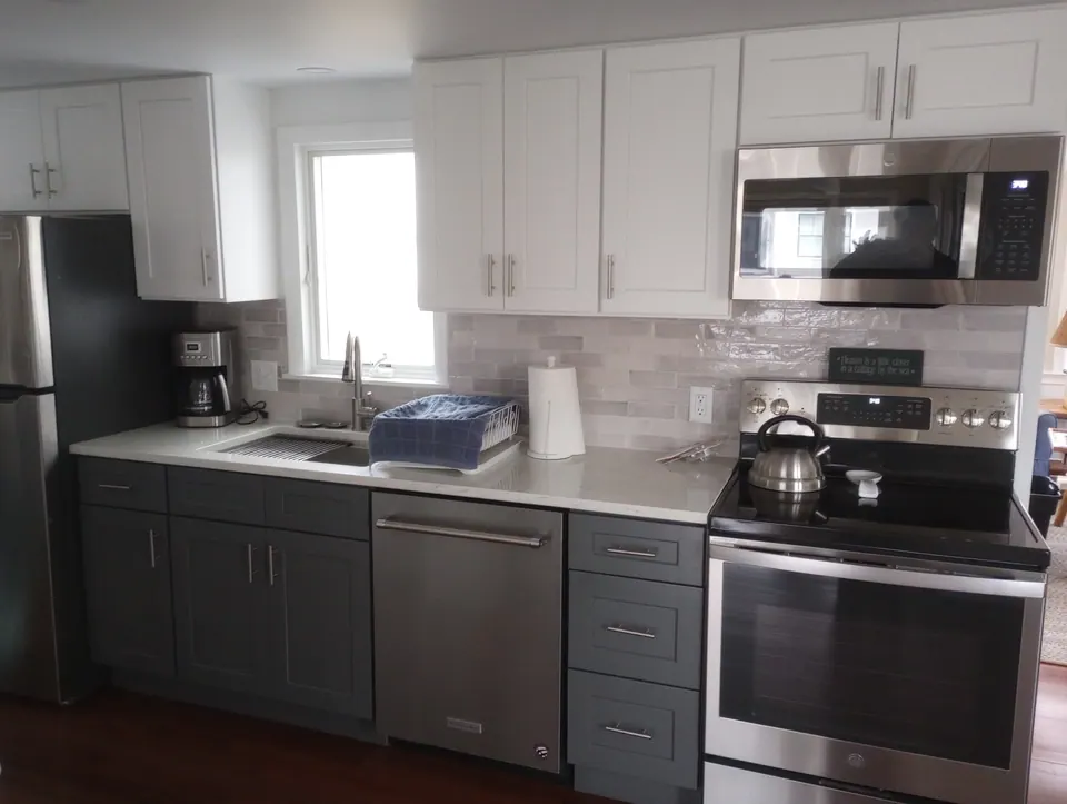 Dark gray base cabinets and white wall cabinets along the sink wall, with refrigerator, dishwasher, microwave and range.