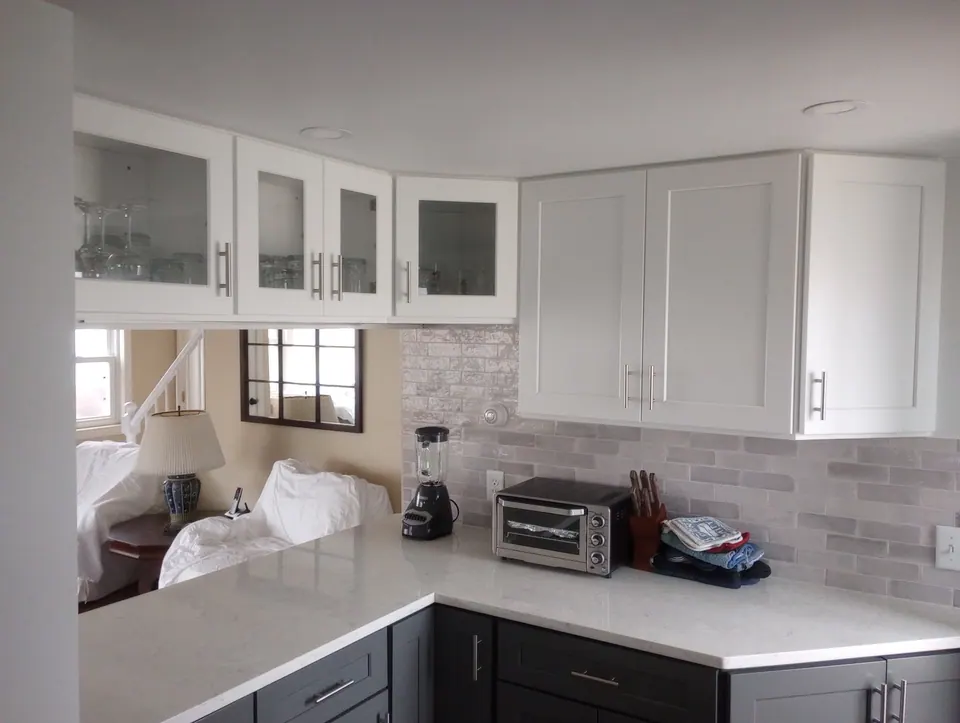 White glass-front and solid wall cabinets over dark gray base cabinets, white counter and gray brick-pattern tile backsplash.